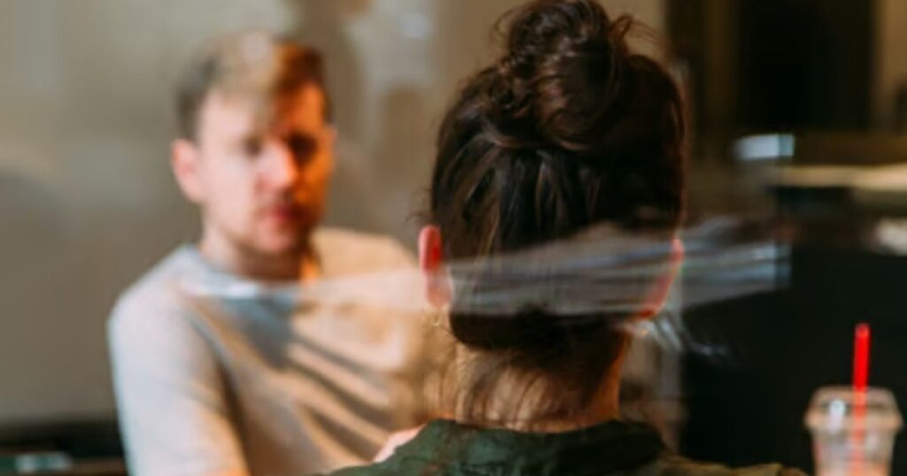 A woman seen from behind in conversation with a man across a café table