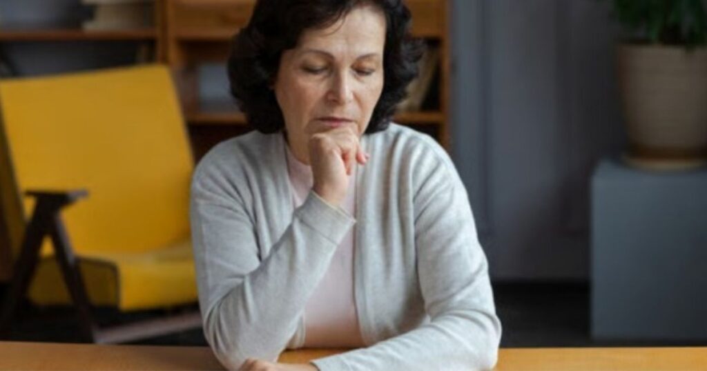 A woman sitting at a table with lowered eyes, resting her chin on her hand in thought